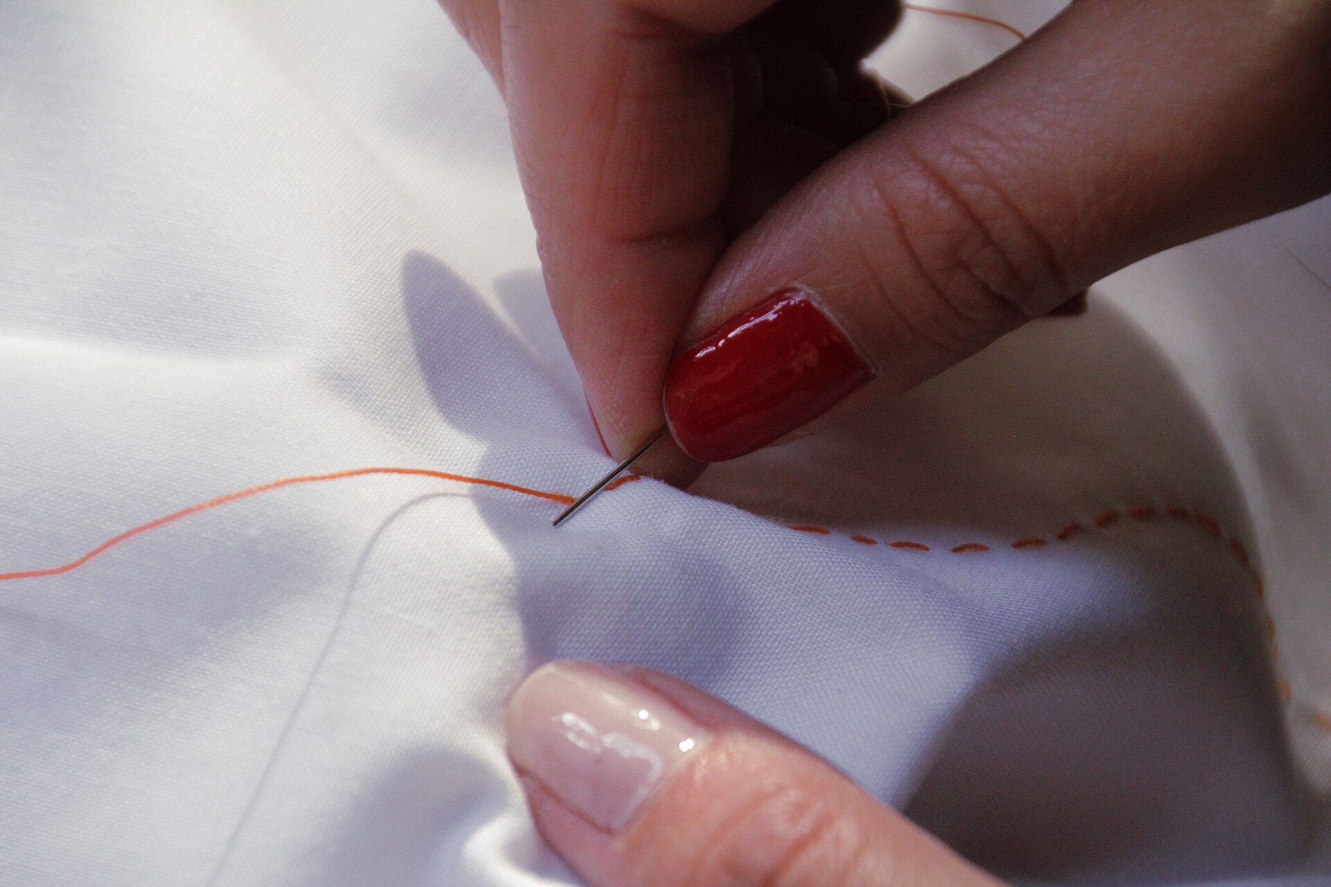 Hands working a line of sashiko running stitches on pale cloth